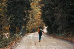 contento viaggio con un' zaino nel un' caldo maglione, i pantaloni e stivali passeggiate lungo il strada nel il autunno foresta foto