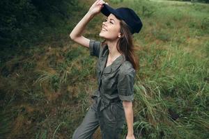 donna nel il foresta guardare su sorridente nero berretto fresco aria viaggio sfondo verde le foglie foto