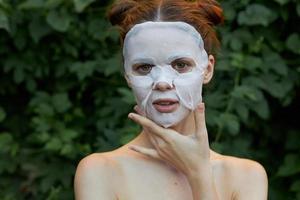 bellissimo donna anti rughe maschera nel natura, lui tocchi il suo viso spoglio le spalle cespugli nel il sfondo foto