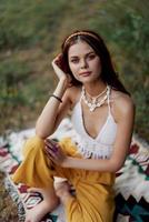 giovane bellissimo hippie donna seduta su il terra nel natura nel il autunno nel eco capi di abbigliamento nel il tramonto luce, un' stile di vita di viaggio e armonia con il mondo foto