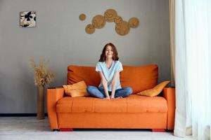donna su il arancia divano nel il riposo camera in posa appartamenti foto