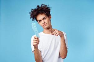 emotivo uomo con un' pettine nel il suo mano e Riccio capelli nel un' blu sfondo copia spazio foto