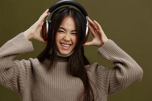 ritratto donna nel un' maglione ascoltando per musica con cuffie divertimento verde sfondo foto