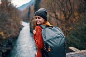 donna turista zaino in spalla su il ponte vicino il fiume autunno foresta montagne foto