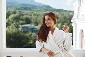 ritratto donna nel un' bianca accappatoio su il balcone po su verde natura montagna Visualizza foto