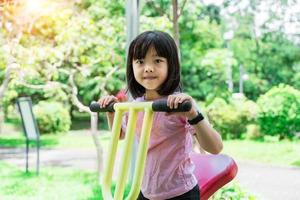 allegro bambino ragazza giocando su terreno di gioco nel il parco. salutare estate attività per bambini. foto