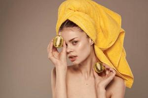 donna con spoglio le spalle con un' asciugamano su sua testa Kiwi nel sua mani pulito pelle frutta cosmetici foto