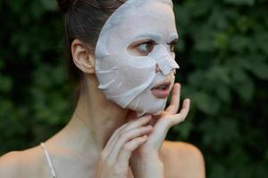 simpatico donna detiene il suo mano vicino il suo viso bianca maschera pelle cura le foglie nel il sfondo foto