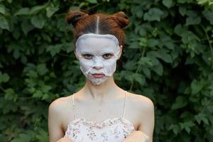 simpatico ragazza cosmetico maschera offeso occhiata verde cespugli pelle cura le foglie nel il sfondo foto