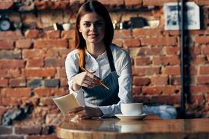 donna Cameriere caffè tazza vicino il tavolo mattone parete foto