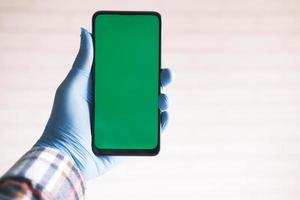 mano in guanti di lattice verde tenendo smart phone con schermo verde foto