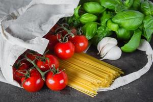 basilico, pomodori ciliegia, aglio nel tessuto Borsa su buio tavolo sfondo. riutilizzabile Borsa con drogheria. foto