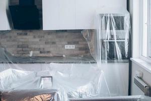 mobilia coperto con plastica su il cucina. riparazione nel appartamento. incompiuto appartamento interno foto