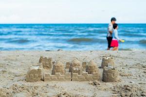 il castello di sabbia costruito dallo stampo con persone sfocate che camminano sulla spiaggia sullo sfondo foto