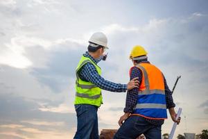 ingegnere e caposquadra che controllano il progetto in cantiere, ingegnere e costruttori in elmetti protettivi che discutono in cantiere, concetti di lavoro di squadra foto