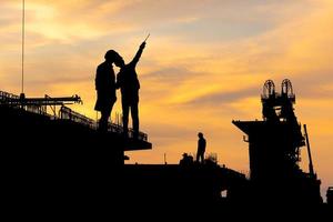 silhouette di ingegnere e caposquadra lavoratore controllo progetto a infrastruttura costruzione luogo, costruzione luogo a tramonto nel sera foto