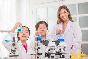 elementare scienza classe, allegro poco bambini con insegnante scienziato mostrando test bottiglia con chimica liquido nel scuola laboratorio, scienza laboratorio foto