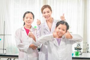 elementare scienza classe, allegro poco bambini con insegnante scienziato mostrando test bottiglia con chimica liquido nel scuola laboratorio, scienza laboratorio foto