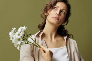 divertente bello irritato Riccio bellissimo femmina nel biancheria casuale camicia hold camomille fiori a parte sembra su in posa isolato su al di sopra di oliva verde pastello sfondo. natura è bellezza concetto. copia spazio foto