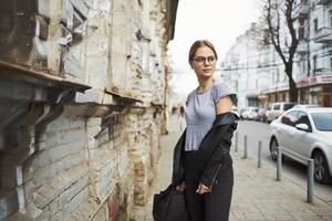 un' bellissimo donna nel un' nero pelle giacca e maglietta sta su il strada vicino il vecchio edificio foto