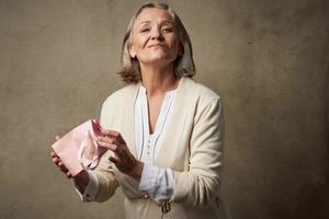 anziano donna nel un' condimento toga con un' regalo nel sua mani compleanno cura foto