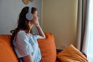 allegro donna ascoltando per musica con cuffie su il arancia divano tecnologie foto