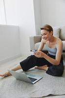 libero professionista donna con il computer portatile e Telefono lavori a partire dal casa seduta su il pavimento nel sua casa Abiti con un' corto taglio di capelli, gratuito copia spazio foto