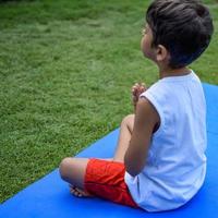 asiatico inteligente ragazzo fare yoga posa nel il società parco all'aperto, figli di yoga posa. il poco ragazzo fare yoga esercizio. foto