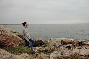 bellissimo donna nel un' grigio maglione sta su un' roccioso riva natura rilassamento concetto foto