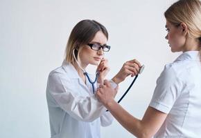 medico nel un' medico toga con un' stetoscopio esamina un' paziente su un' leggero sfondo foto