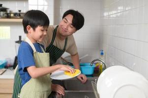 contento sorridente giovane asiatico padre e figlio lavaggio piatti nel cucina a casa foto