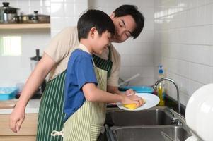 contento sorridente giovane asiatico padre e figlio lavaggio piatti nel cucina a casa foto