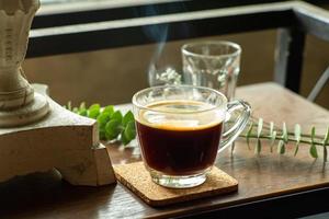 primo piano un bicchiere di caffè nero caldo con fumo sul tavolo di legno foto