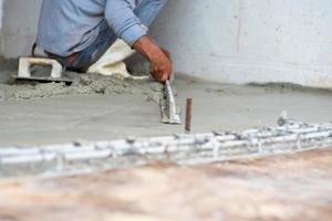messa a fuoco selettiva sulle mani dei lavoratori che utilizzano la cazzuola di legno che appiattisce la superficie del pavimento di cemento foto