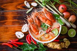 tailandese cibo tom yum kung, caldo e acida speziato gamberetti gamberi la minestra curry Limone lime galangal rosso chili cannuccia fungo su tavolo cibo, gamberetto la minestra su frutti di mare la minestra ciotola con tailandese erba e spezie foto