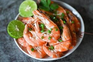 gamberetto su bianca bolw e di legno sfondo cenare tavolo cibo, fresco gamberetti gamberi frutti di mare Limone lime con erbe aromatiche e Spezia foto