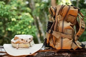 secchio cappello e zaino escursioni a piedi con un' torcia elettrica riposo su di legno legname nel il sfondo è un' foresta foto