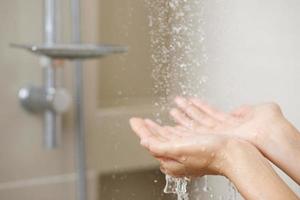 un' donna usi mano per misurare il acqua temperatura a partire dal un' acqua riscaldatore prima assunzione un' doccia foto