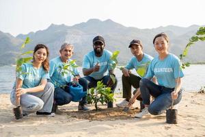 gruppo di volontario sorridente per telecamera seduta su il spiaggia. protezione di ambiente e natura, ecologia concetto. foto