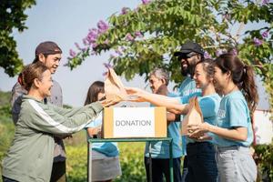 squadra di volontari sorridente e Tenere donazioni scatole nel all'aperto. volontari mettendo cibo nel donazione scatole, sociale lavoratore fabbricazione Appunti beneficenza foto