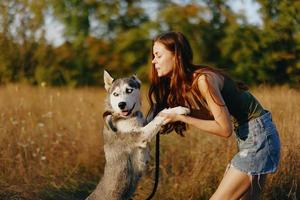 un' snello donna giochi e balli con un' rauco razza cane nel natura nel autunno su un' campo di erba e sorrisi a un' bene sera nel il ambientazione sole foto