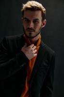 ritratto di un attraente biondo uomo su un' buio sfondo nel un arancia maglione e cappotto foto