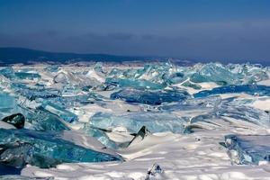 grande ghiaccio hummocks di trasparente ghiaccio su lago baikal. il ghiaccio è verde e blu. montagne su il orizzonte. buio blu cielo. foto