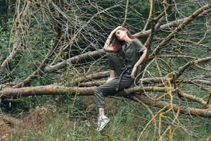 un' donna nel un' verde tuta tocchi sua testa e si siede su un' rotto albero foto