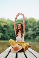 un' hippie donna si siede su un' ponte di un' lago su un' natura viaggio e sorrisi nel eco-abbigliamento. il concetto di eco-attivista e natura conservazione foto