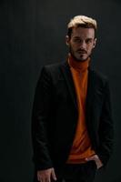biondo uomo nel un' cappotto e un arancia maglione su un' buio sfondo davanti Visualizza modello foto