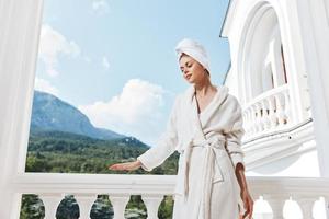 ritratto donna con un' asciugamano su mio testa nel un' bianca accappatoio soggiorno su il balcone nel un' Hotel montagna Visualizza foto