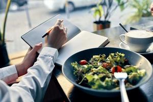 delizioso cibo insalata nel un' piatto forchetta bloc notes con il iscrizione e donna nel camicia bar interno foto