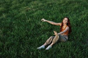 un' giovane donna è giocando nel il parco con noi nel il erba e cascate per il terra sorridente felicemente nel il luce del sole. riposo nel natura, armonia con il corpo foto