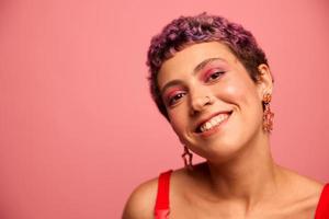 moda ritratto di un' donna con un' corto taglio di capelli di viola colore e un' Sorridi con denti nel un' rosso superiore su un' rosa sfondo danza felicemente foto